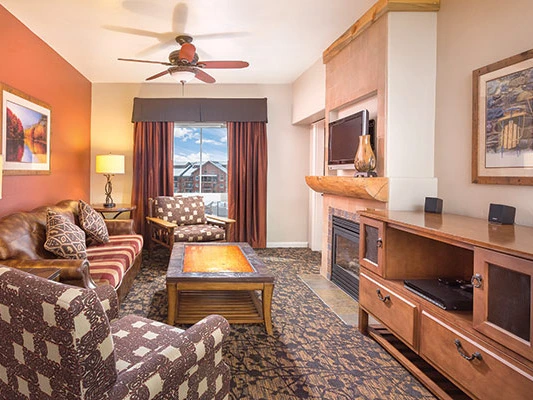 Cozy resort living room interior featuring patterned seating, a rustic stone fireplace, a coffee table, and a flat-screen television.