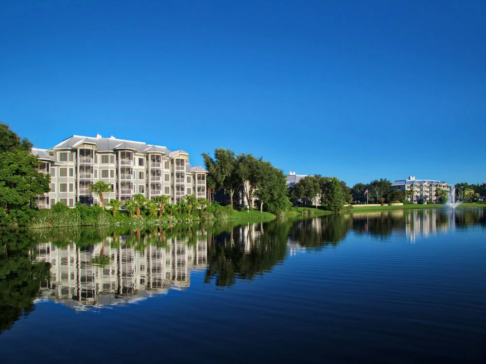 Waterfront view of Marriott Cypress Harbour reflecting in calm water with clear blue sky.