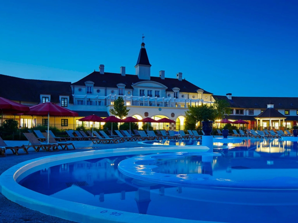 Marriott Timeshare Costs Image: Marriott Village d'ile-de-France's luxurious hotel pool at night, with red umbrellas and lounge chairs beside it, reflecting bright lights.