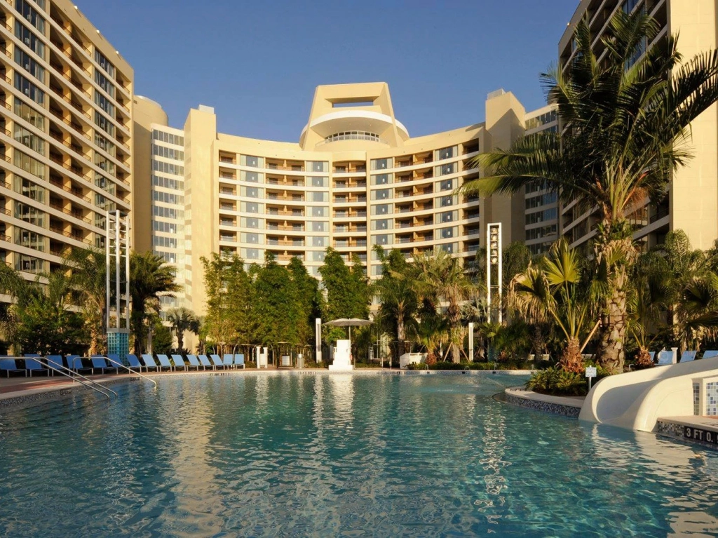 Large swimming pool and water slide in front of the curved Bay Lake Tower at Disney's Contemporary Resort.