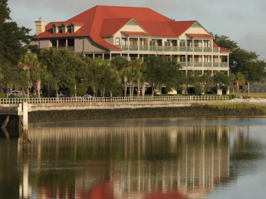Multi-story resort building with a red roof reflecting on the calm water at sunset.
