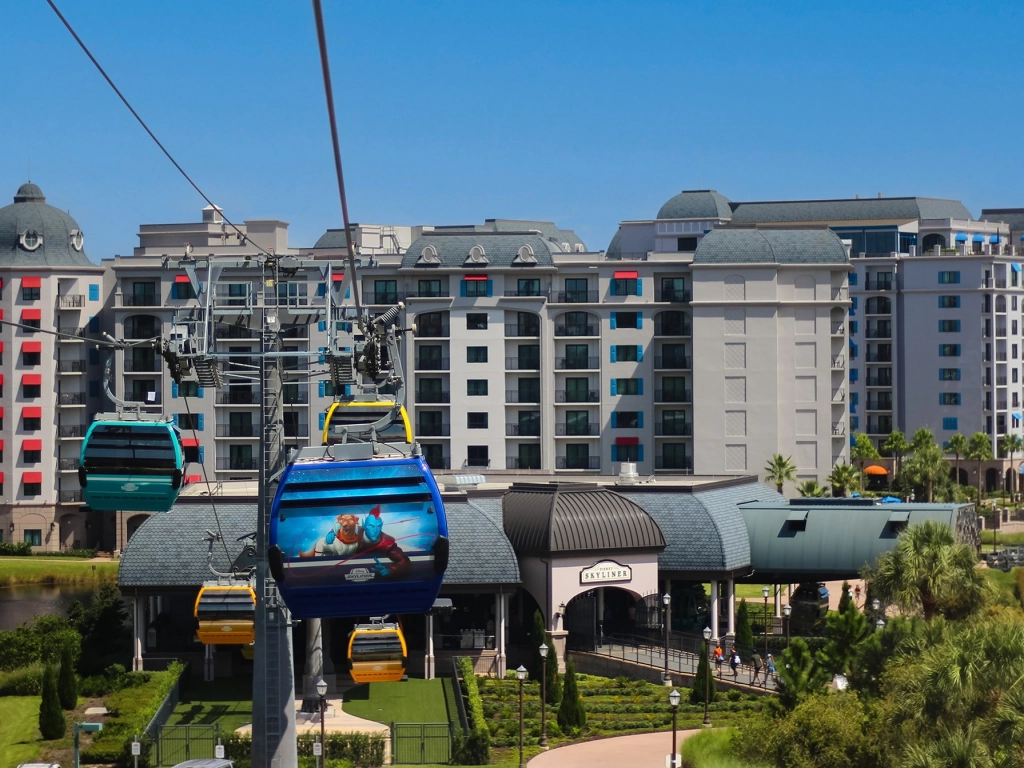 Blue and yellow Disney Skyliner gondolas pass in front of the grand, European-styled Disney's Riviera Resort building. - why are timeshare resales so cheap?