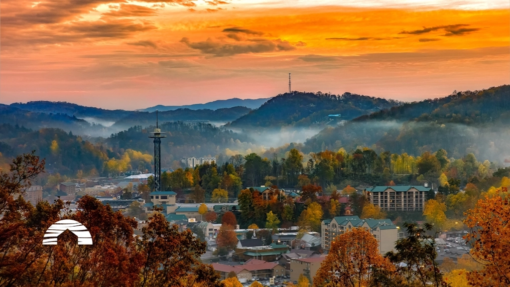Vibrant sunset over Gatlinburg, Tennessee, with autumn foliage, mountain fog, and the Space Needle towering above the town.