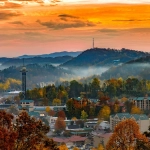 Vibrant sunset over Gatlinburg, Tennessee, with autumn foliage, mountain fog, and the Space Needle towering above the town.