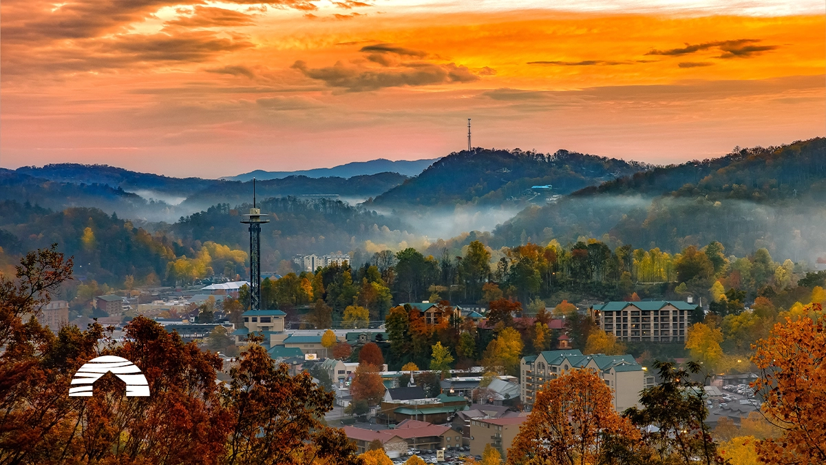 Vibrant sunset over Gatlinburg, Tennessee, with autumn foliage, mountain fog, and the Space Needle towering above the town.