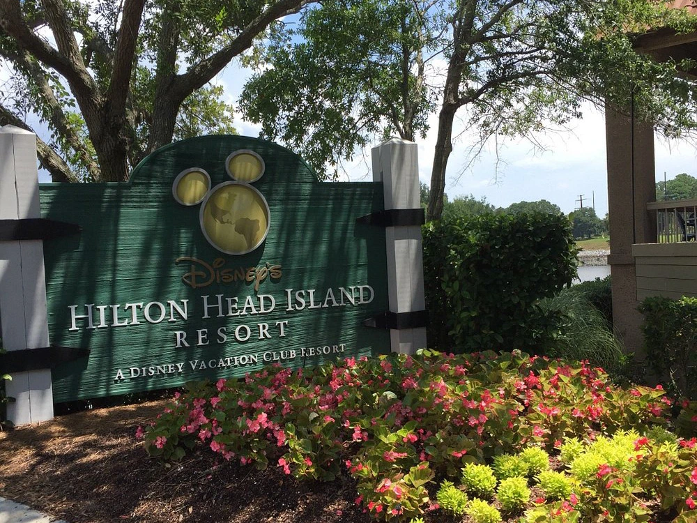 Wooden entrance sign for Disney's Hilton Head Island Resort surrounded by pink flowers.