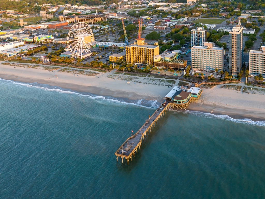 Aerial view of the sandy coastline, wooden pier, and large Ferris wheel.