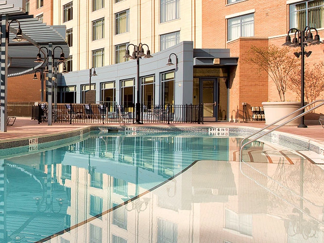 Outdoor swimming pool reflecting a brick resort building with a patio and lounge chairs.