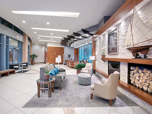 Modern resort lobby featuring a seating area, front desk, and a fireplace with a decorative sailboat.