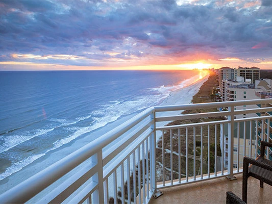 Oceanfront balcony view overlooking the sandy coastline and ocean waves at sunset from a timeshare in Myrtle Beach.