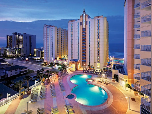 Illuminated outdoor pools and high-rise resort towers at dusk at Wyndham Ocean Boulevard.