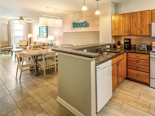 Suite kitchen with wood cabinets, granite counters, and a living area at a timeshare in Myrtle Beach.