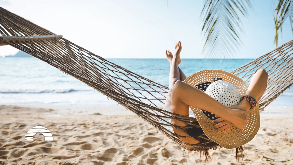 Person relaxing in a hammock on a sandy beach looking at the ocean during a summer vacation.