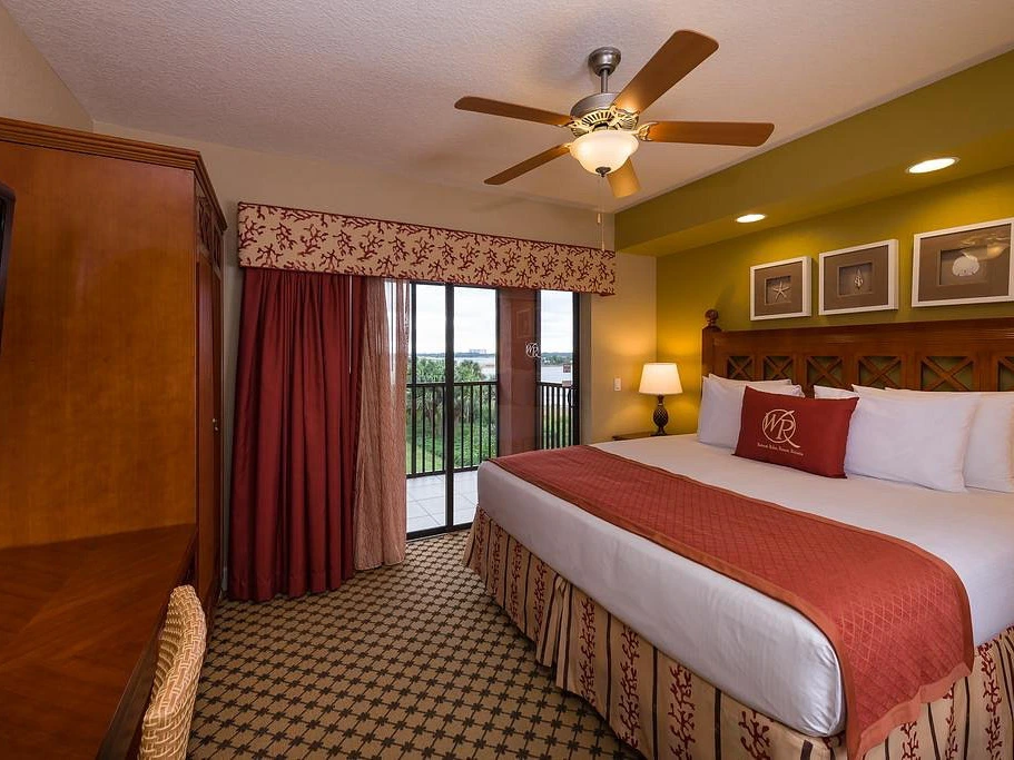 King bedroom with red bedding, wood furniture, and sliding doors to a lakeview balcony at Westgate Lakes Resort and Spa.