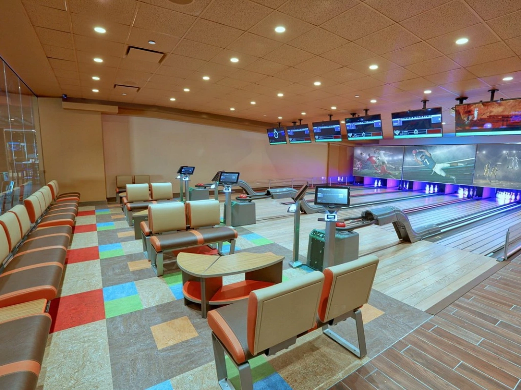 Indoor bowling alley featuring colorful carpet, lounge seating, and screens above lanes.