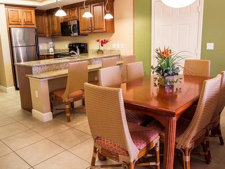 Open kitchen and dining area with a long wood table, wicker chairs, and modern appliances.