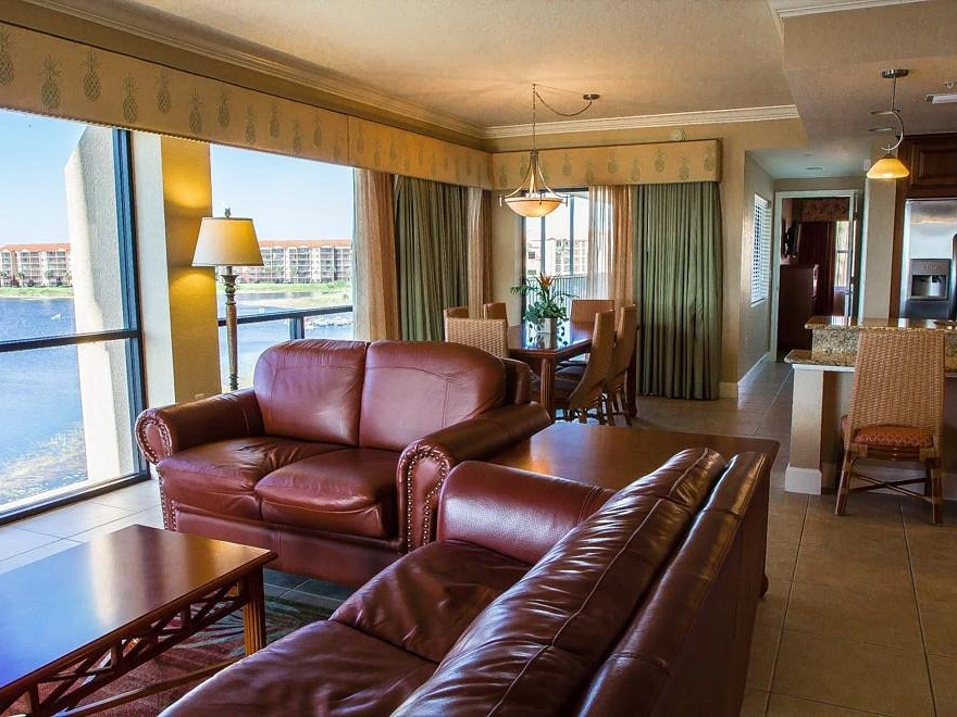 Living room with brown leather sofas, large windows overlooking a lake, and an adjacent dining area.