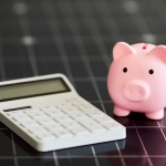 A pink piggy bank next to a white calculator on a black grid background, symbolizing financial savings.