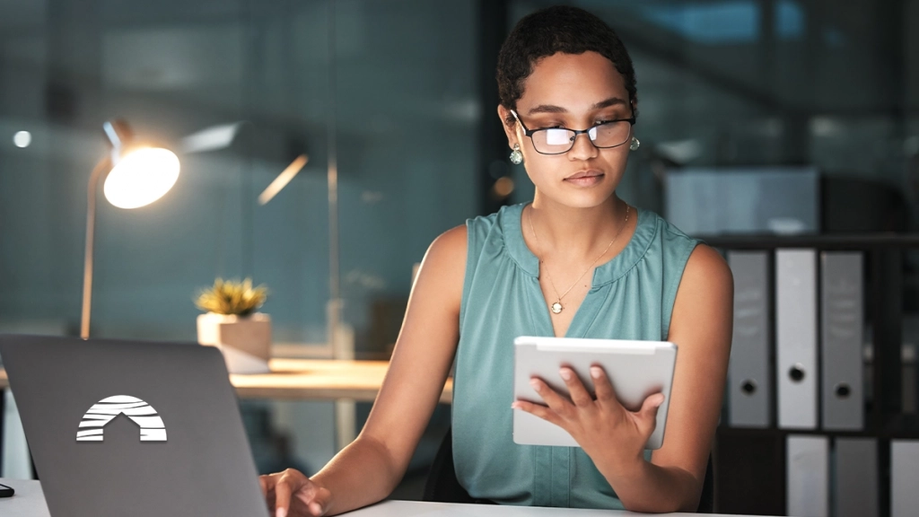 Woman researching a timeshare deedback on her tablet and laptop in a dark office.
