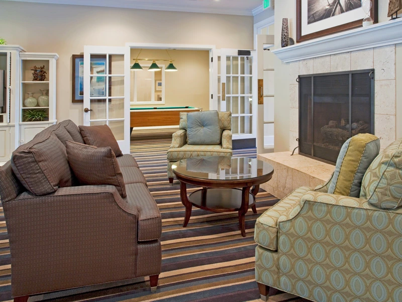 Cozy resort lounge with a fireplace, patterned armchairs, and a view of a billiards room.