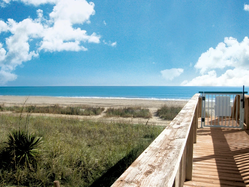 A perfect summer vacation view of a wide sandy beach and blue ocean from a wooden boardwalk.
