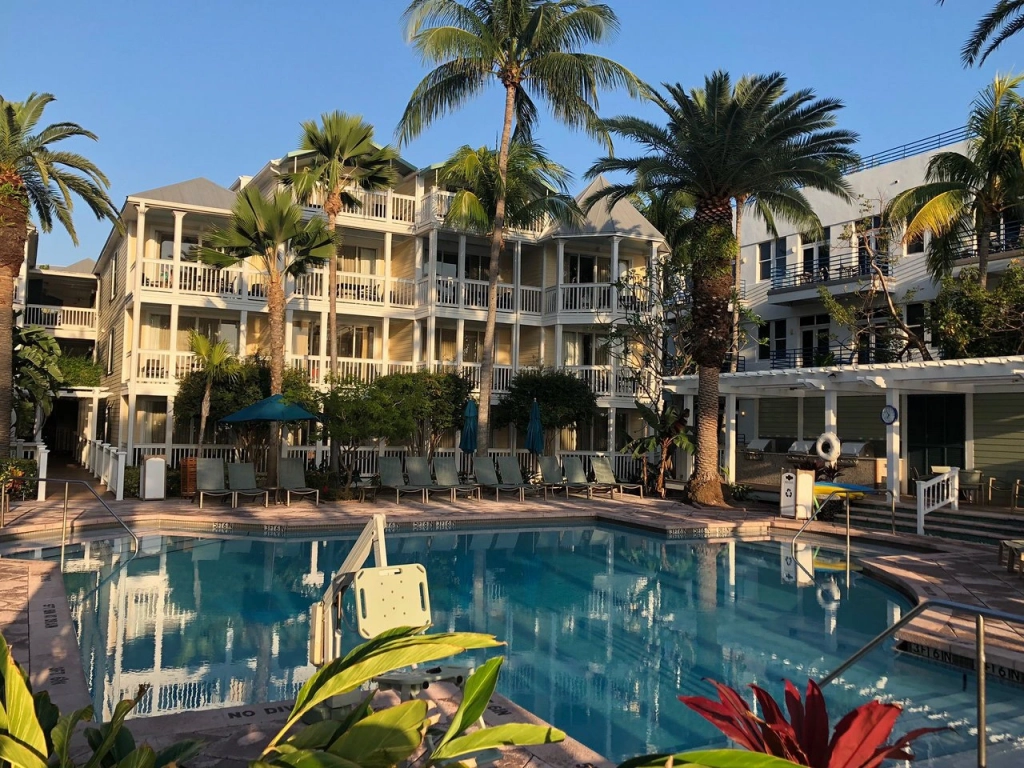 Palm trees surround a pristine resort swimming pool with a yellow, multi-story plantation-style guest building behind it. - why are timeshare resales so cheap?