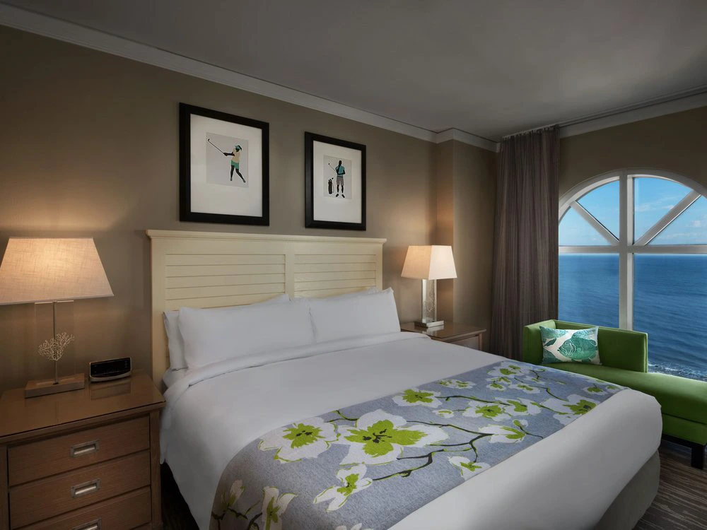Master bedroom with a king bed, green chaise, and an arched ocean view window at a timeshare in Myrtle Beach.
