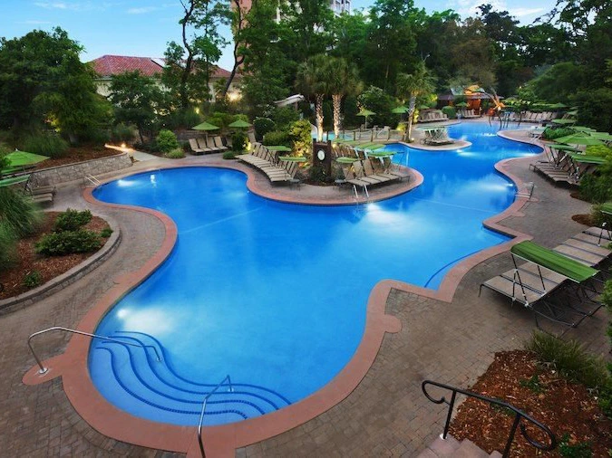 Large outdoor pool surrounded by lounge chairs and trees at a timeshare in Myrtle Beach.
