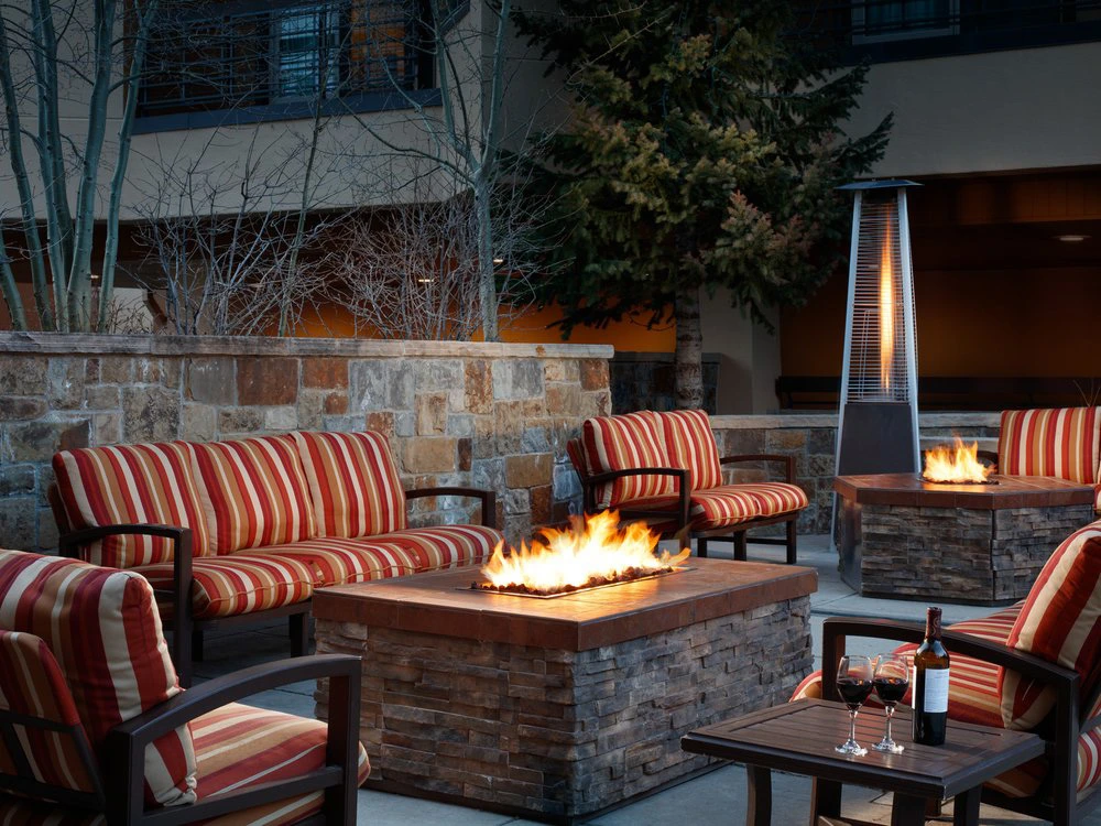 Comfortable outdoor lounge chairs with red and gold stripes surround blazing stone fire pits at a mountain resort patio.