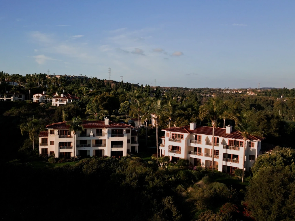Aerial view of white buildings with red tile roofs nestled among lush green trees at Four Seasons Aviara.