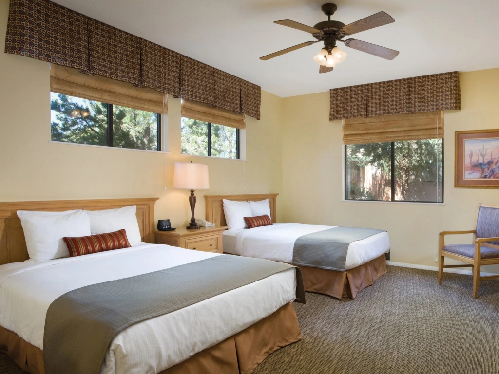 A bright bedroom at a Timeshare in Sedona featuring two beds, large windows with valances, and a ceiling fan.