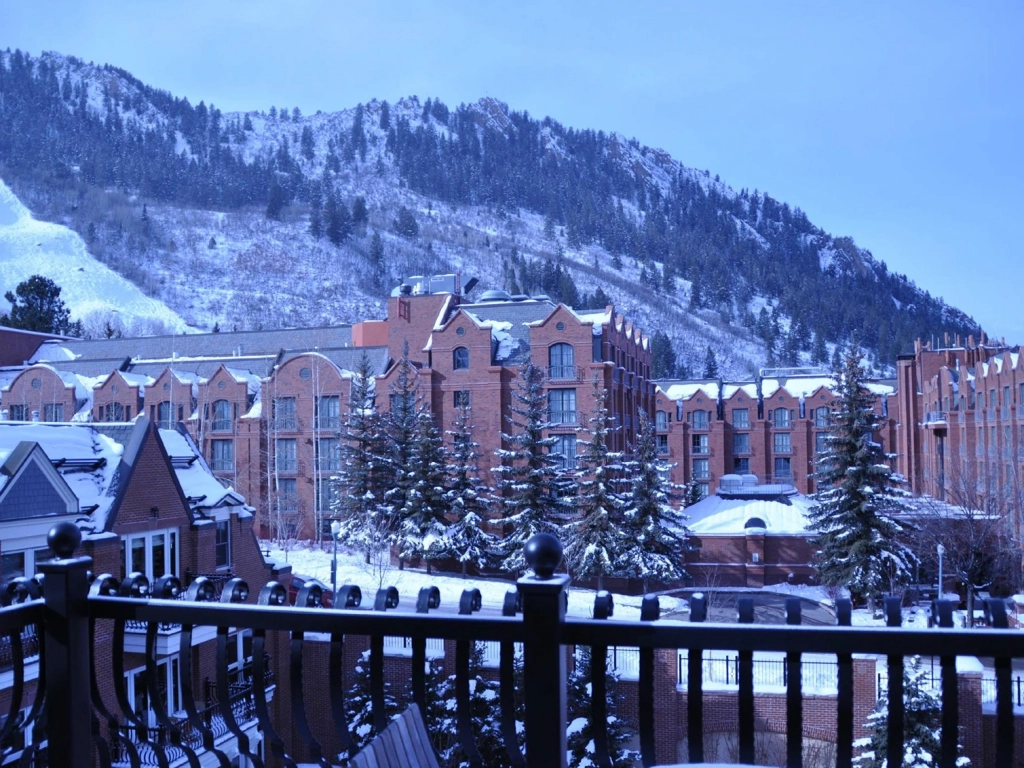Exterior view of the brick Hyatt Grand Aspen resort buildings covered in winter snow with mountains in the background.