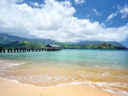 Calm blue ocean waters and a long wooden pier extending from a sandy KaEoKai beach.