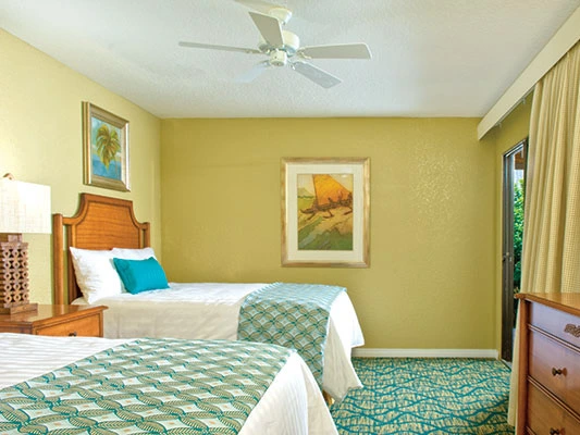 Guest bedroom featuring two twin beds with teal accents, patterned carpet, and framed wall art.