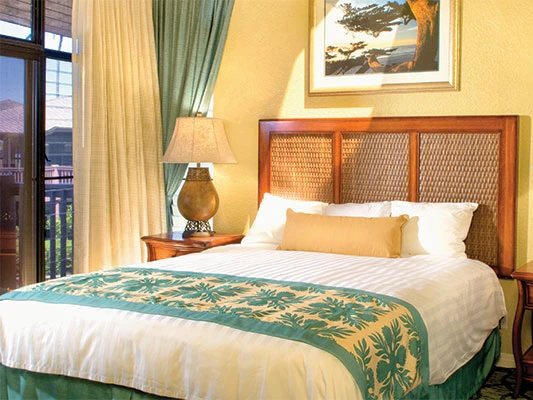 Master bedroom with a woven headboard, tropical bed runner, and sliding glass balcony doors.