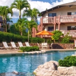 Tropical resort pool surrounded by natural rock formations, lush greenery, and patio umbrellas.