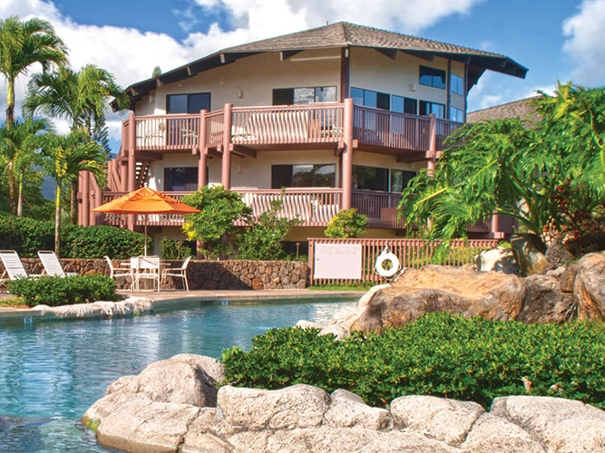 Tropical resort pool surrounded by natural rock formations, lush greenery, and patio umbrellas.