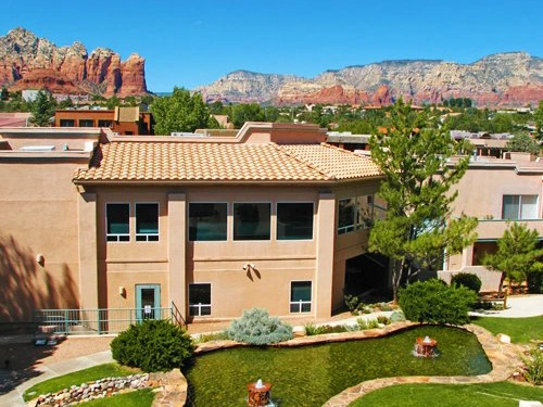 Tan stucco resort buildings surround a landscaped courtyard with a small fountain and red rock mountain views.
