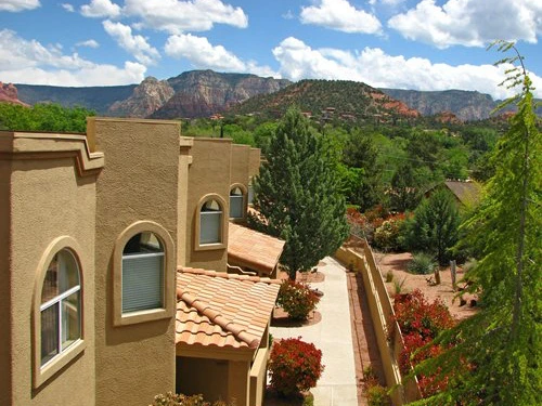 A paved walkway winds past tan resort buildings with red tile roofs toward towering mountains at a Timeshare in Sedona.