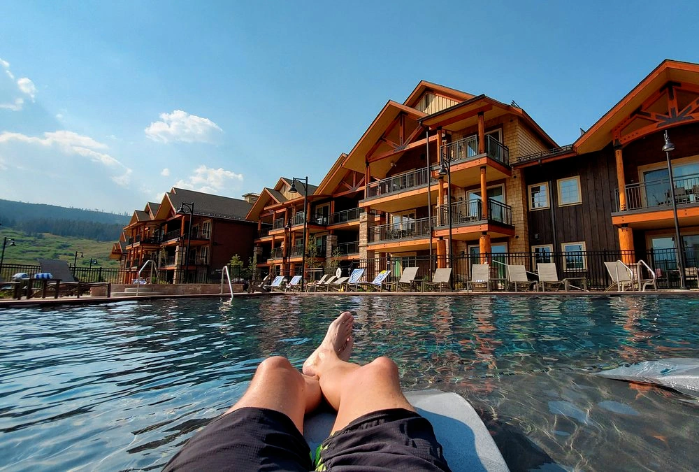 A guest relaxes on a pool floatie looking toward the rustic wooden balconies of The Ranahan resort in Breckenridge.