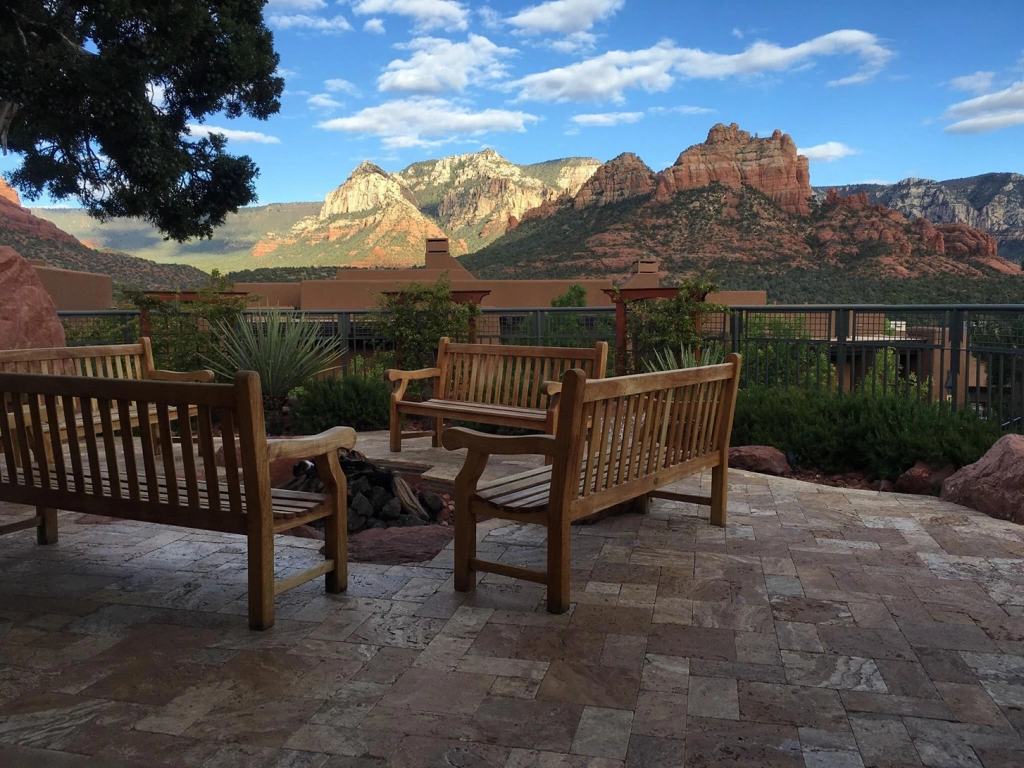 Wooden benches surround a stone fire pit patio at a Hyatt Vacation Club resort with beautiful red rock mountain views.