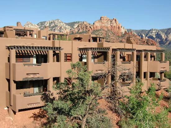 Exterior of a tan stucco resort building with private balconies, set against a backdrop of towering red rock formations.