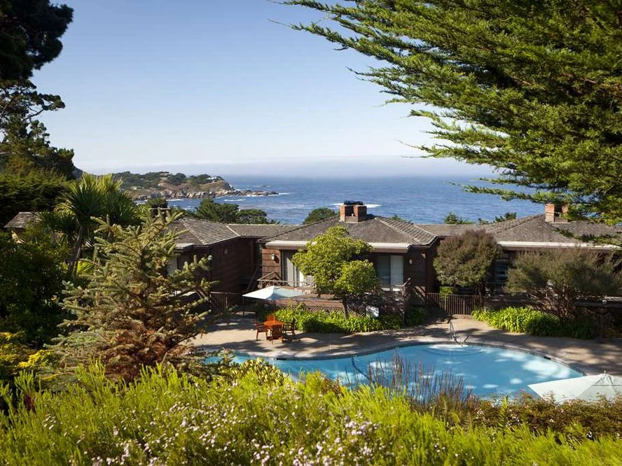 A swimming pool surrounded by lush greenery overlooks the scenic ocean coast at the Hyatt Highlands Inn in Carmel.