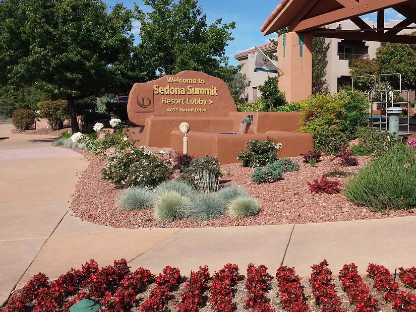 A landscaped entrance featuring a red rock monument, water feature, and vibrant flowers at a Timeshare in Sedona.