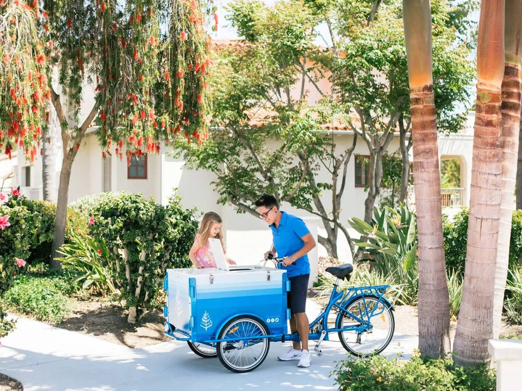Staff member serving a child from a blue cargo bike cart at a timeshare in San Diego resort grounds.