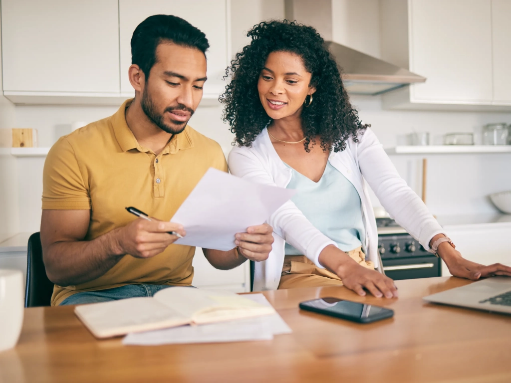 Couple reviewing an estoppel certificate at kitchen table with laptop and phone nearby.
