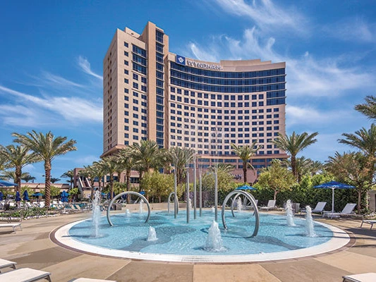 Large curved hotel building and a foreground splash pad at the Wyndham Desert Blue resort.