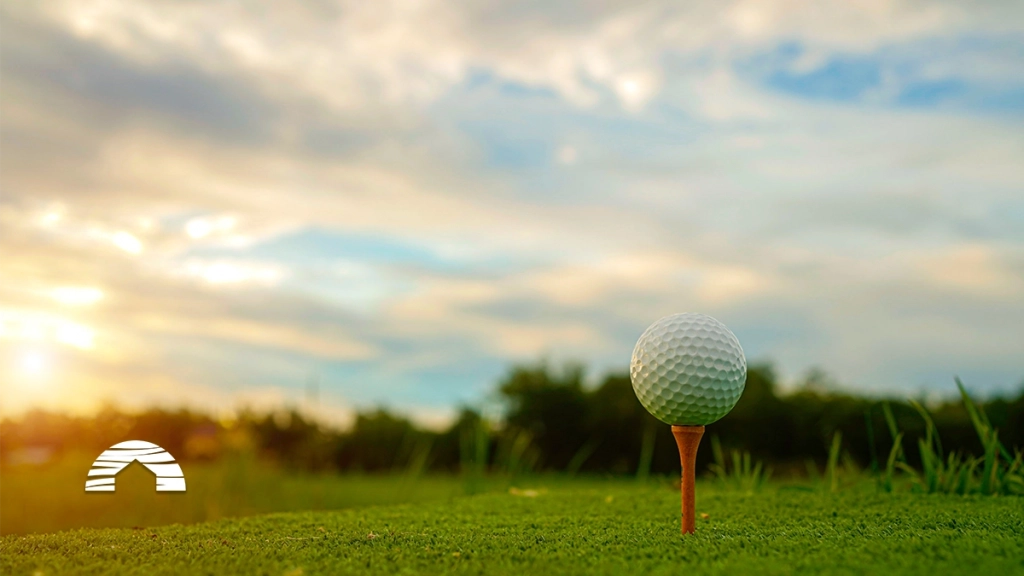 Close-up of a golf ball on a wooden tee with a blurred golf course background at sunset.