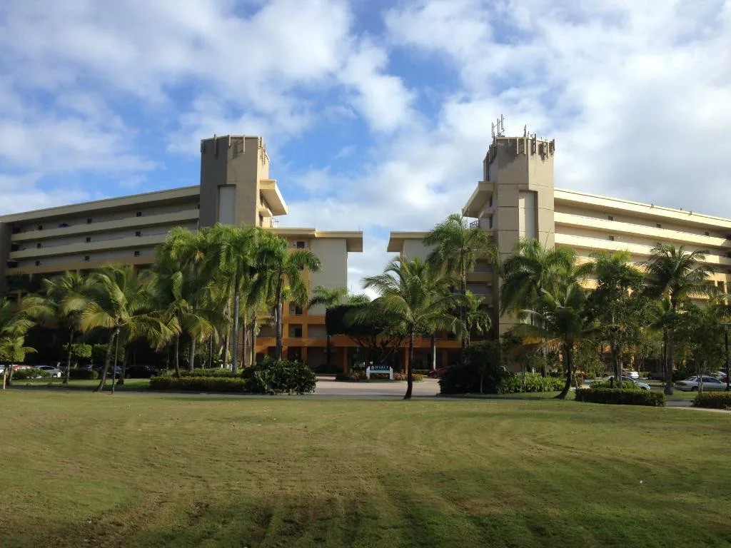 Lush palm trees and manicured lawns frame a two-wing hotel.
