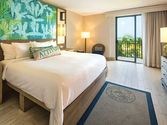 Bright timeshare in Puerto Rico with king bed, tropical wall art, and a balcony overlooking palm trees and ocean.